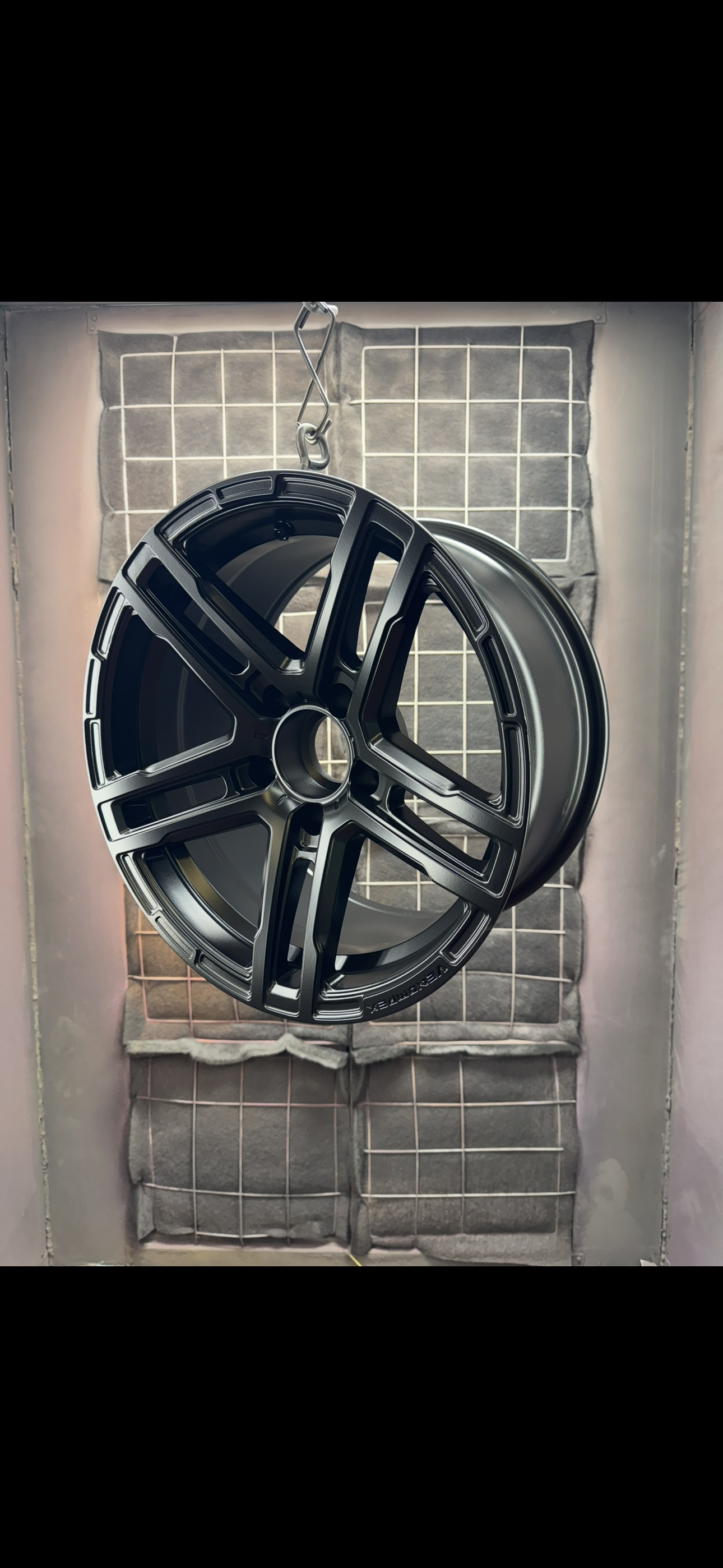A black car wheel rim hanging in a spray paint booth.